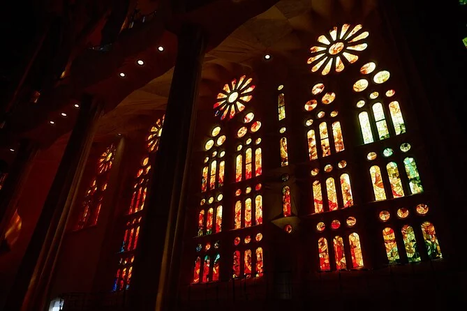 Rote, orangefarbene und gelbe Buntglasfenster, die im abgedunkelten Inneren der Sagrada Familia leuchten